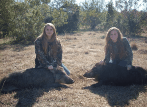 Two female hunters, each sitting with a harvested Florida Hog